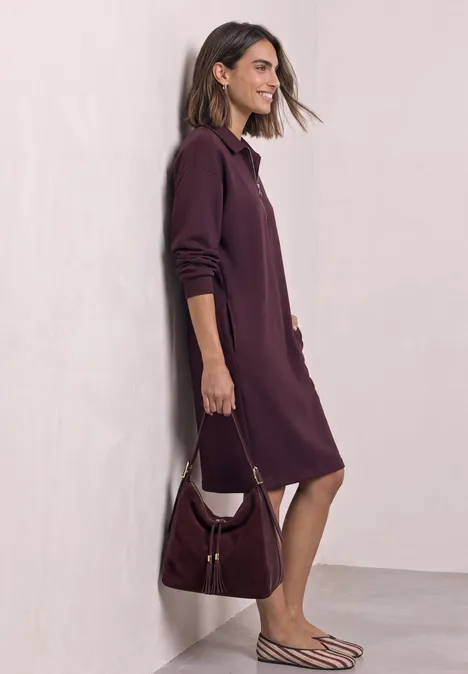 Femme de profil portant une robe-chemise violet foncé, un sac à épaule assorti et des sandales rayées.