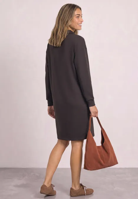 Femme vue de dos portant une robe sombre mi-longue, sac cabas marron et mocassins beiges.