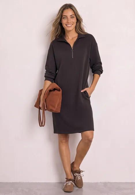 Femme en robe sweat noire à demi-zip, poches et accessoires marron, style décontracté.