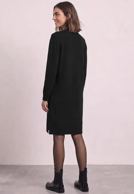 Femme en robe noire et bottines regarde par-dessus l’épaule