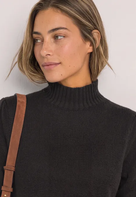 Portrait d'une femme en pull noir à col montant, regard de côté