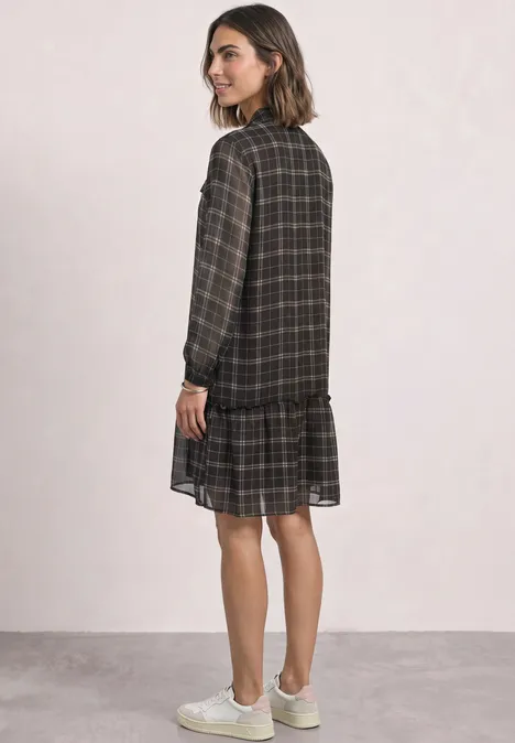 Knielanges Tunikakleid mit Schleifendetail black coffee Eine Frau trägt ein knielanges, kariertes Langarmkleid mit Rüschensaum und weiße Sneaker.