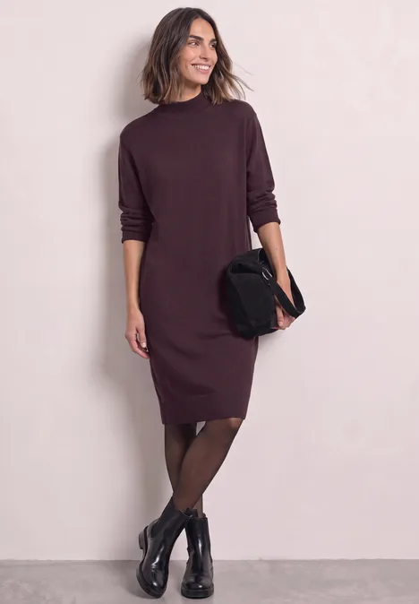 Femme en robe pull bordeaux à manches longues, collants noirs, bottines et pochette noire.