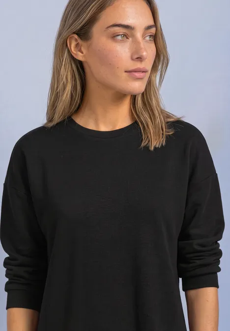 Femme en pull noir uni regardant sur le côté, fond neutre.