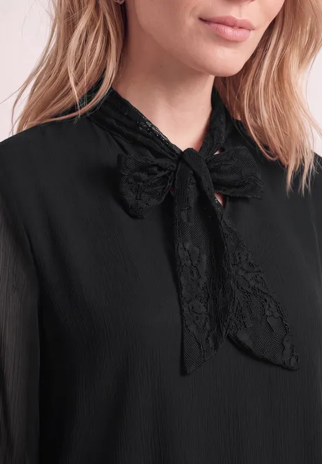 Close-up van een vrouw in een zwarte blouse met een fijne kanten strik bij de hals.