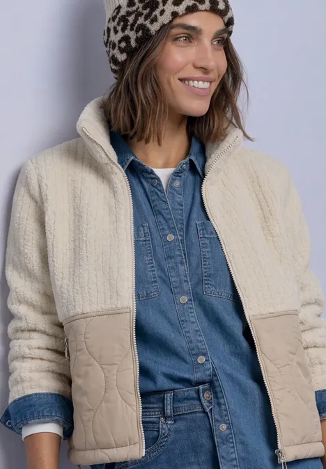 Teddyjas met softshell-details Soft Fawn Beige Frau in hellem Teddy-Fleece-Jacke, Jeanshemd und Leopardenmütze lächelt.