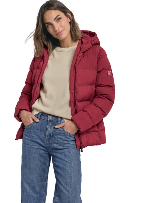 Frau trägt rote Daunenjacke, hellen Pullover und blaue Jeans