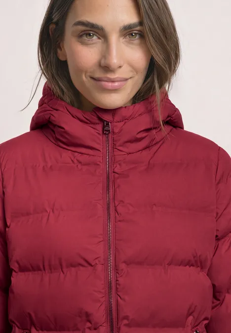 Nahaufnahme einer Frau in roter Steppjacke mit Kapuze, die leicht lächelt.