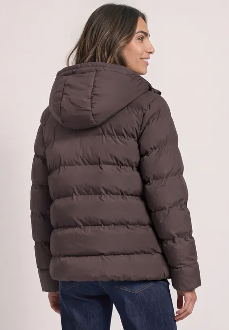 Kurze Jacke mit geklebter Steppung plummy brown Rückansicht einer Person in brauner Steppjacke mit Kapuze und blauen Jeans vor hellem Hintergrund.
