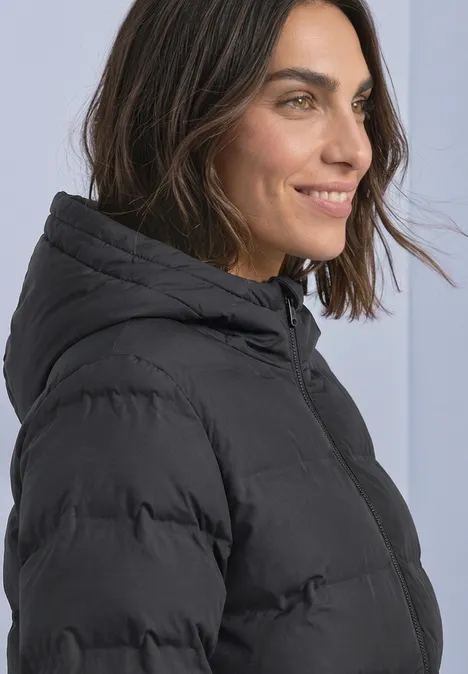 Kurze Jacke mit geklebter Steppung Obsidian Blue Eine Frau in schwarzer Steppjacke mit Kapuze blickt lächelnd zur Seite.