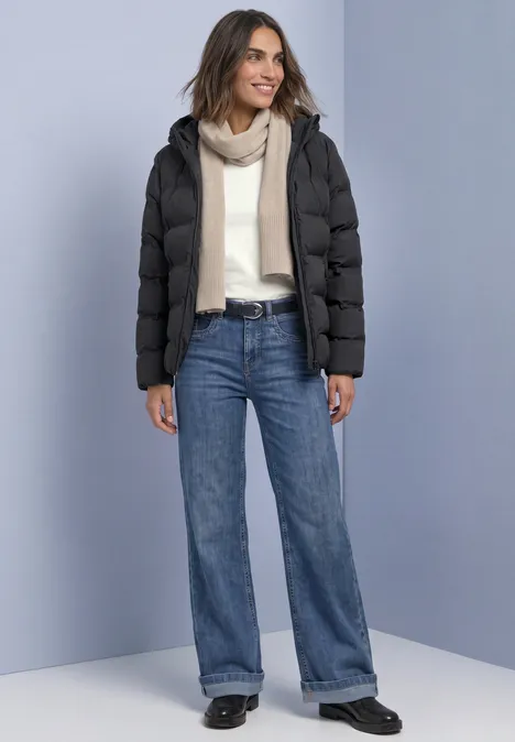 Kurze Jacke mit geklebter Steppung Obsidian Blue Frau trägt schwarze Daunenjacke, hellen Pullover, Schal und weite Jeans.