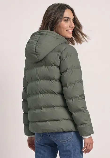 Kurze Jacke mit geklebter Steppung Somber Green Frau in khakigrüner Steppjacke mit Kapuze und Jeans, schaut lächelnd über die Schulter.