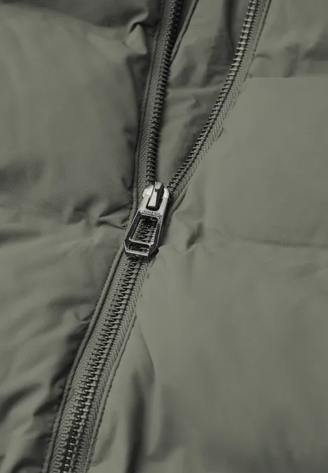 Kurze Jacke mit geklebter Steppung Somber Green Nahaufnahme eines olivgrünen Steppjacken-Reißverschlusses.