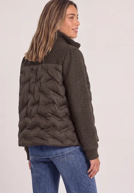 Vrouw van achteren in modieuze jas met gewatteerde achterkant en gebreide mouwen, gecombineerd met jeans.
