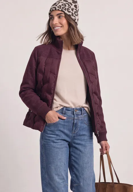 Femme en doudoune bourgogne, jean et bonnet, tenant un sac.