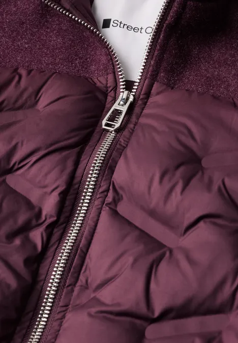 Gros plan d'une veste matelassée bordeaux avec fermeture éclair métal et col polaire.