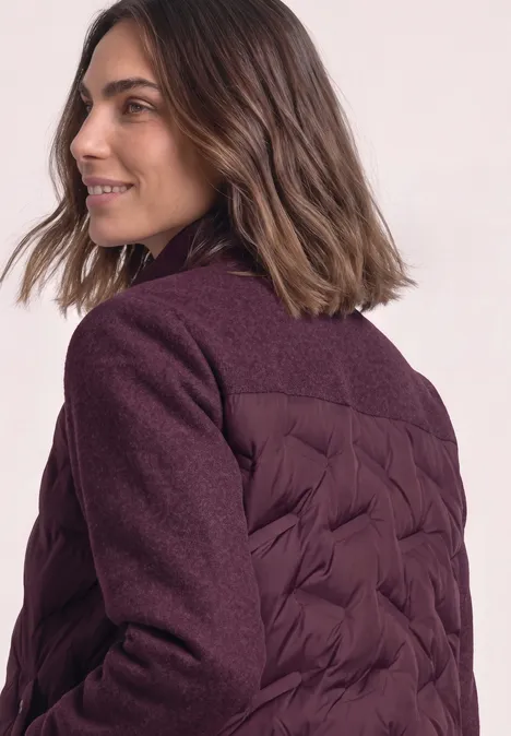 Une femme portant une veste matelassée prune, souriante et regardant sur le côté.