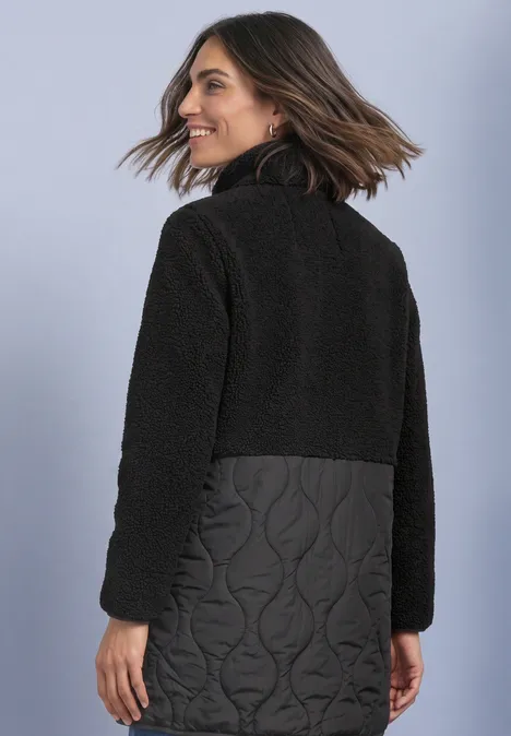 Mantel mit Strukturmix und Stehkragen Black Frau von hinten mit schwarzer Jacke, obere Hälfte Fleece, untere Hälfte gesteppter Stoff mit Wellenmuster.