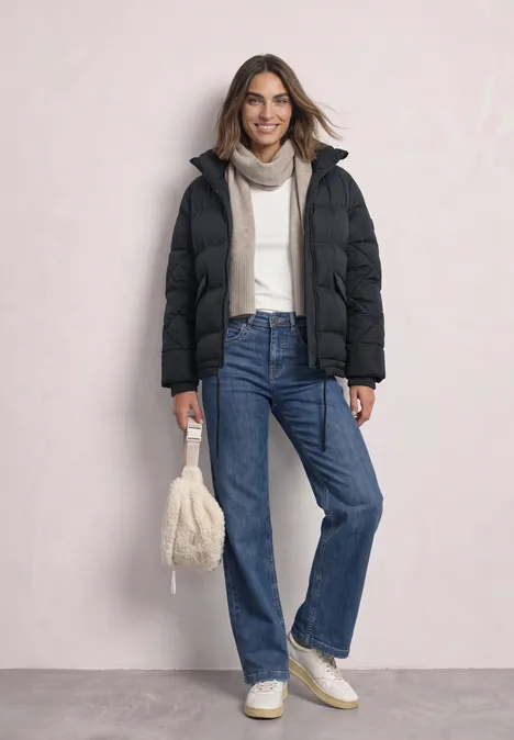 Dame trägt winterliche Daunenjacke, Jeans und Beanie, hält weiße flauschige Tasche.