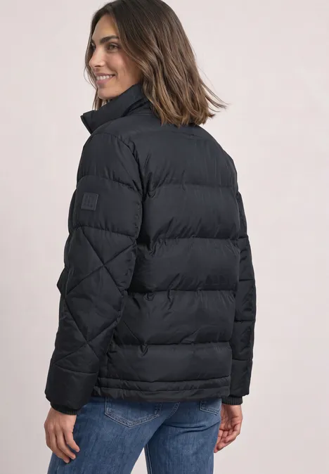 Frau von hinten in schwarzer Steppjacke und blauer Jeans, sie lächelt über die Schulter.