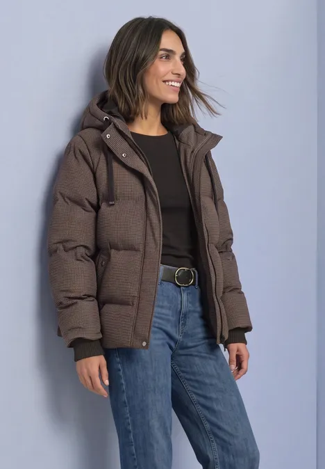 Jacke mit Kapuze und Steppmuster auburn brown Frau mit brauner Daunenjacke, schwarzem Shirt und blauen Jeans lächelt seitlich.