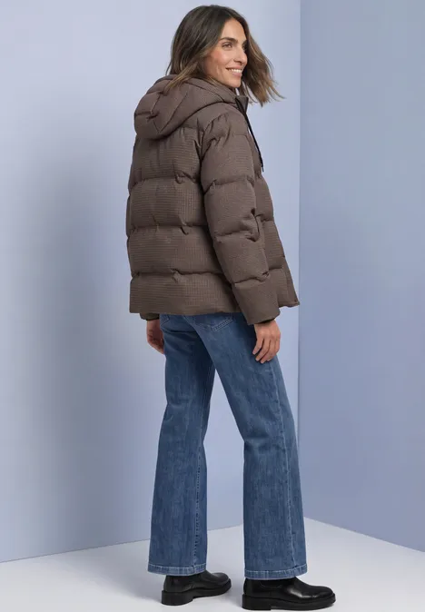Jacke mit Kapuze und Steppmuster auburn brown Frau in brauner Steppjacke mit Kapuze, Jeans und schwarzen Schuhen, schaut lächelnd über die Schulter.