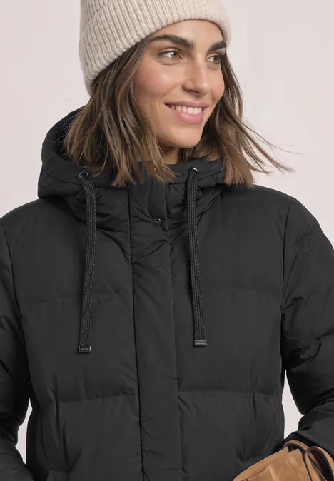 Vrouw met beige gebreide muts en zwarte gewatteerde jas, winterse look.