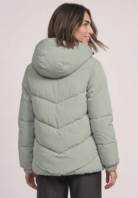 Puffer Jacke mit Teddyfutter in der Kapuze Fresh Sage Frau von hinten in hellgrüner Steppjacke mit Kapuze.