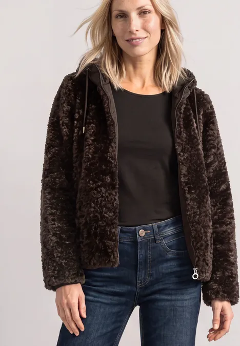 Frau trägt braune, flauschige Jacke, schwarzes Shirt und Jeans