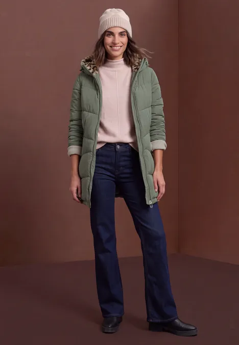 Gevoerde parka met nepbont in luipaardprint Somber Green Frau in grünem Wintermantel mit Kapuze, heller Mütze, Pullover, dunkler Jeans und schwarzen Stiefeln.