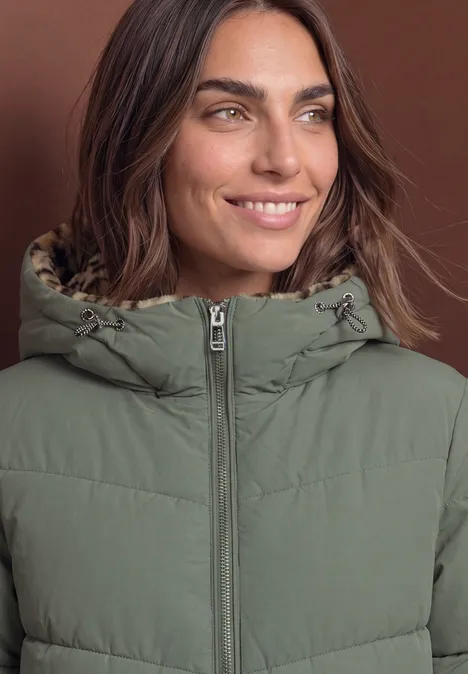 Gevoerde parka met nepbont in luipaardprint Somber Green Eine lächelnde Frau trägt eine grüne, gesteppte Jacke mit Kapuze vor braunem Hintergrund.