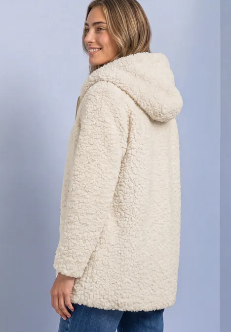 Femme portant un manteau sherpa crème à capuche, vue de côté sur fond bleu clair.