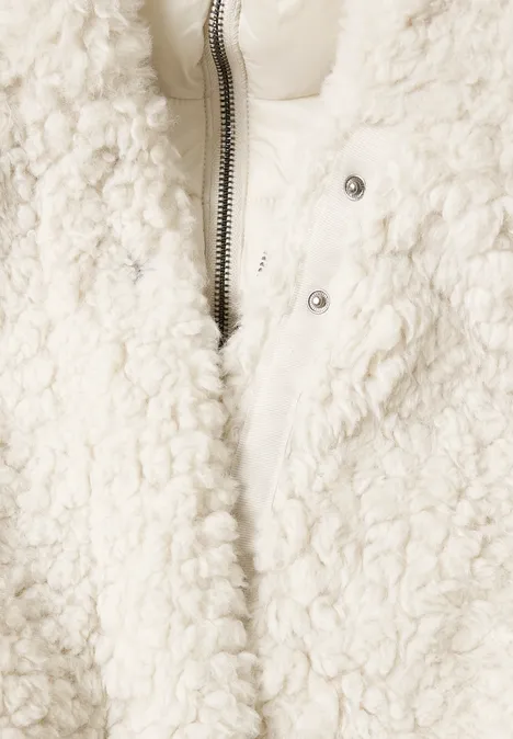 Gros plan sur une veste teddy crème avec fermeture éclair et boutons-pression.