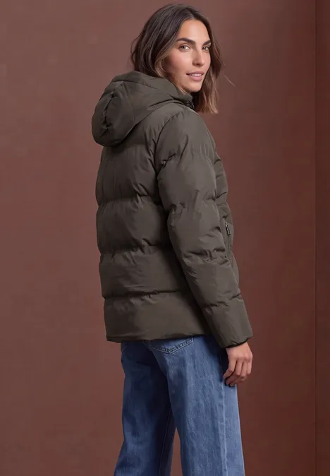 Vrouw in donkergroene gewatteerde jas en blauwe jeans kijkt over haar schouder.