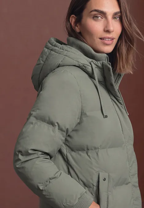 Lange Jacke mit Kapuze und Steppmuster Somber Green Frau in hellgrüner, gesteppter Kapuzenjacke vor schlichtem Hintergrund.