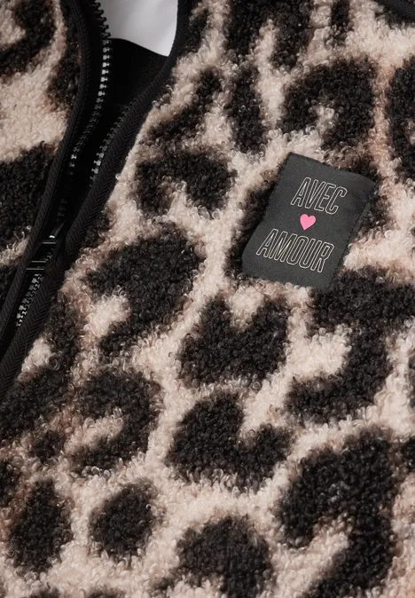 Zbliżenie na pluszową tkaninę w lamparcie cętki z zamkiem błyskawicznym i naszywką 'Just Be Kind'.