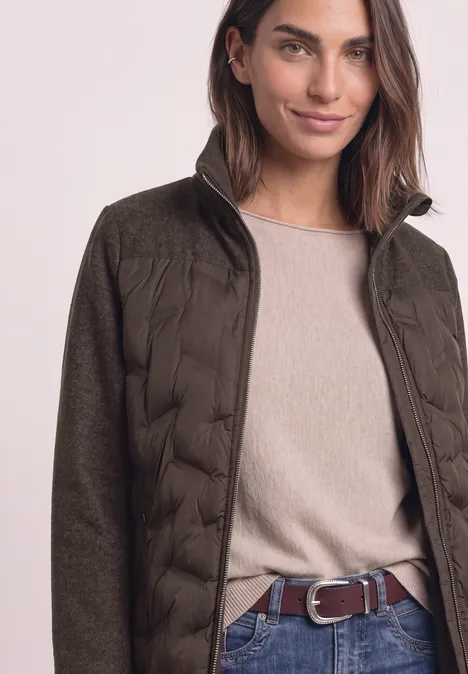 Frau in olivgrüner Steppjacke mit beigem Pullover und braunem Gürtel.