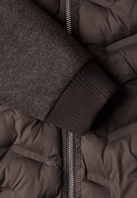 Nahaufnahme eines dunkelgrauen Steppmantels mit Reißverschluss und einem Strickbündchen