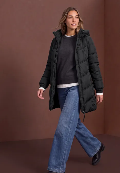 Vrouw in zwarte, gewatteerde winterjas en jeans loopt zelfverzekerd.