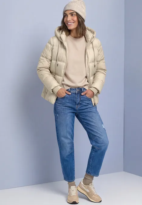 Veste matelassée à capuche barley beige Femme portant doudoune beige, bonnet, jeans bleus et baskets sur fond neutre.