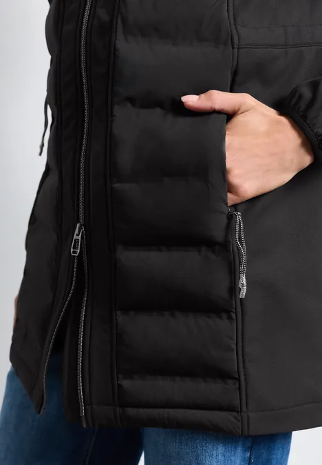 Schwarze, gesteppt Winterjacke mit Reißverschluss, die Hand steckt in der seitlichen Tasche.