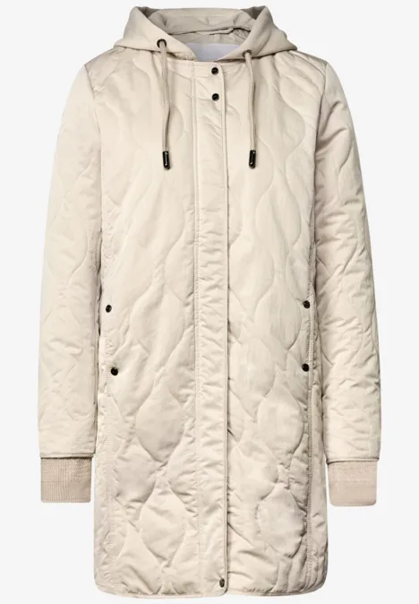 Veste matelassée beige à capuche, fermeture éclair, boutons-pression, poches et poignets côtelés.
