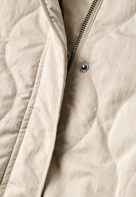 Gros plan d'une veste matelassée beige clair avec fermeture éclair et bouton-pression visibles.