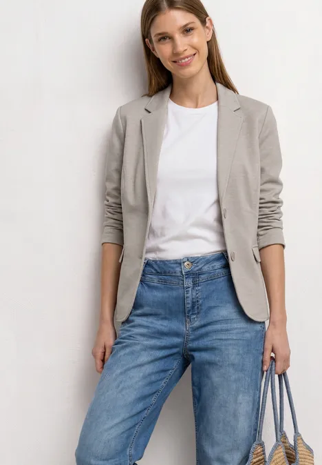 Basic Piqué Blazer clay sand Frau in grauem Blazer, weißem T-Shirt, blauen Jeans und hellblauer Tasche vor weißem Hintergrund.
