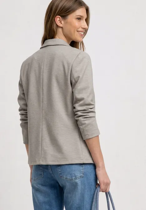 Basic Piqué Blazer clay sand Eine Person von hinten, trägt hellgrauen Blazer, blaue Jeans und hält eine Tasche.