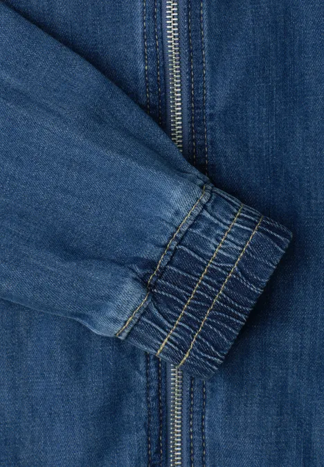 Close-up van een blauwe spijkerjasmouw met ritssluiting en elastische manchetrand.