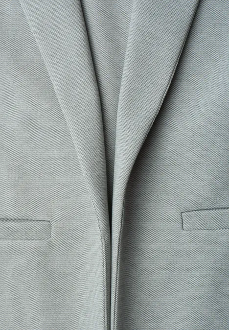 Nahaufnahme eines hellgrauen Blazers mit leichten Falten und dezenten Taschen.