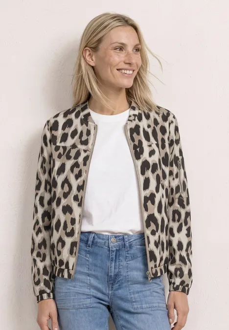 Femme blonde porte une veste bomber léopard, t-shirt blanc et jean bleu sur fond clair.