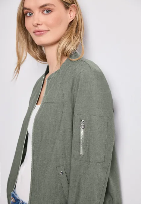 Frau in grüner Bomberjacke mit Reißverschlusstasche am Ärmel und weißem Top