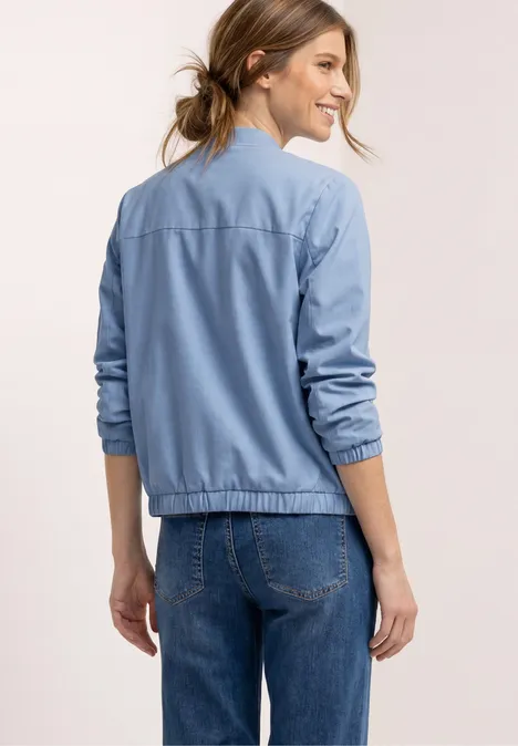 Frau von hinten in blauer Bomberjacke und Jeans stehend.